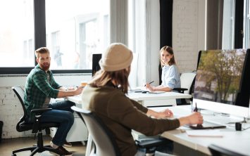 Picture of young colleagues work in office using computers. Looking aside.