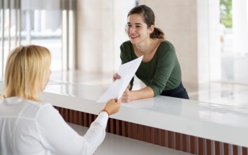 Front desk lady offering tourist to fill out documents. Receptionist giving papers to smiling hotel guest. Hotel and check in concept